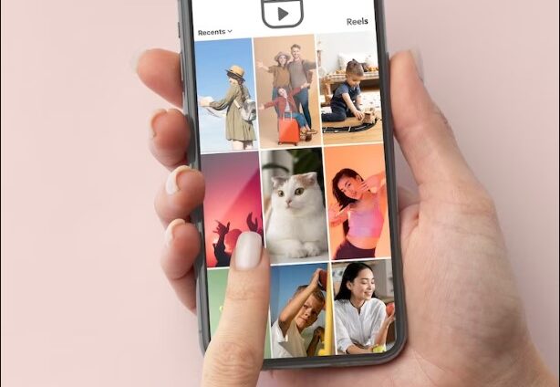 A hand holding a smartphone showing a grid of social media reels with various images.